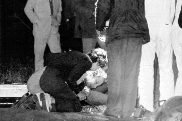 Peter Farr, kneeling over the borehole, talks to his son Billy as a female relative and rescue workers look on. 