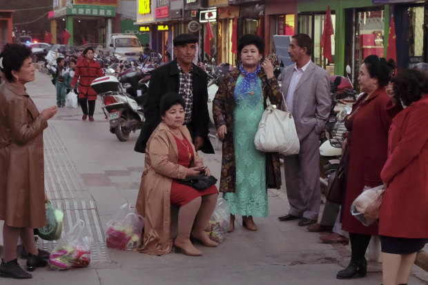 A group of older Turpan locals wait, in western dress, in front of a market.