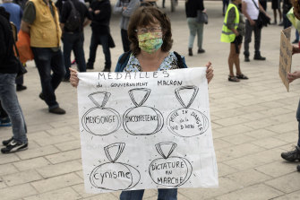 A woman holds a sign reading in French "Macron's government medals: lies, incompetence, endangering the lives of others, cynicism, dictatorship on the move" during a protest in Marseille's Old Port, in France.