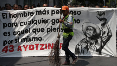 A city cleaner walks past a banner reading, in Spanish, "The most dangerous man for any government is he who thinks for himself," as students demonstrate outside where President-elect Andres Manuel Lopez Obrador was meeting with parents of college students on the fourth anniversary of the students' disappearance. 