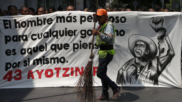 A city cleaner walks past a banner reading, in Spanish, "The most dangerous man for any government is he who thinks for himself," as students demonstrate outside where President-elect Andres Manuel Lopez Obrador was meeting with parents of college students on the fourth anniversary of the students' disappearance. 