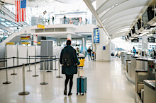 Female traveler arriving to the airport in New York, USA, pushing a stroller bag.