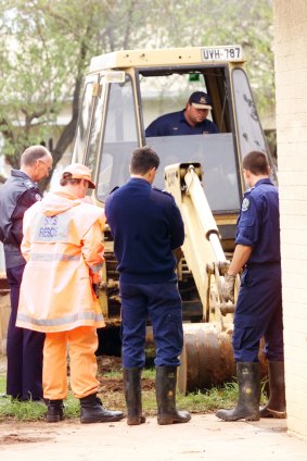 Police watch as a backhoe digs up the yard where another body was found.