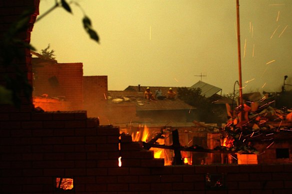 Duffy residents in Canberra sit on the roof of a surviving house while they watch surrounding homes smoulder, 2003.