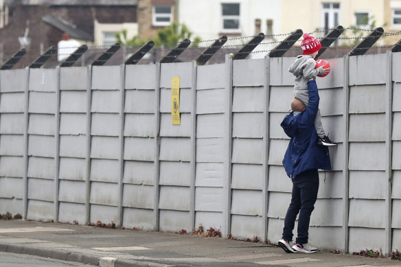 A man helps a child look over the fence at Liverpool's training ground, Melwood. EPL clubs have returned to training after the coronavirus shutdown.