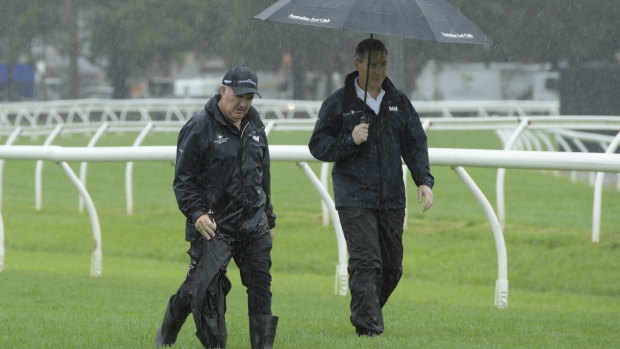 Racing NSW chief steward Marc Van Gestel (with umbrella) and racetrack manager Mark Jones inspect a sodden Warwick Farm.