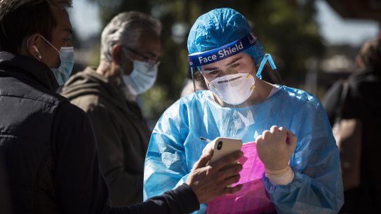 CORONA VIRUS: A woman in full PPE takes down details as people queue along Ninth Street in Campsie to get tested at a Covid Testing Clinic. Campsie in South West Sydney is one of the Sydney hotspots, 30 July 2021. Photo: Jessica Hromas
