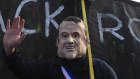 A protester wearing a mask of French President Emmanuel Macron gestures in front of a banner against BlackRock. 