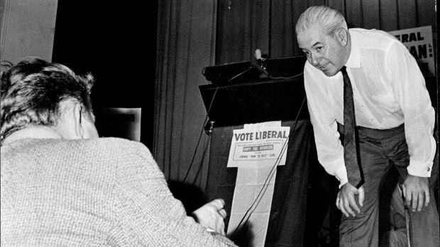 An interjector at a crowded and noisy election meeting comes to the platform to put a question to Mr Holt.