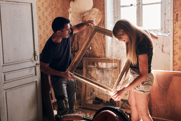 Holding and Selkirk moving picture frames in the water-damaged former staff quarters, a 19th-century chair at their feet. 