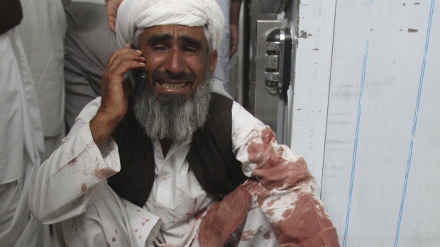 A man talks on a phone sitting next to a body of his family member killed in the attack, in Quetta.