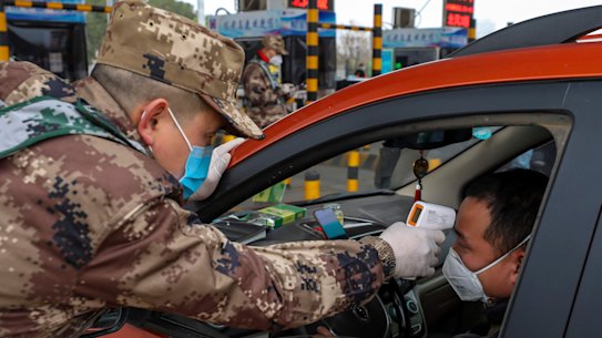 A militia member takes a driver's temperature at a checkpoint at a highway toll gate in Wuhan.
