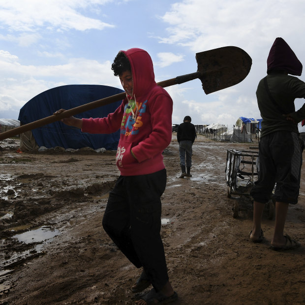 Children carry tools through the mud at the squalid al-Hawl camp.