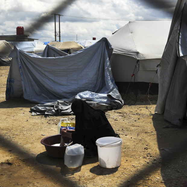 A woman washes clothes in front of her tent at the fence line of the Foreign section of al-Hawl camp in Syria.