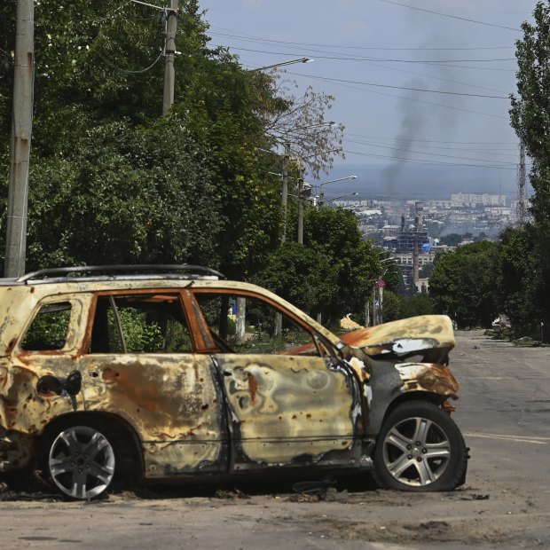 The remains of a vehicle on a road in Lysychansk where smoke can be seen rising from the besieged city of Sievierodonetsk.