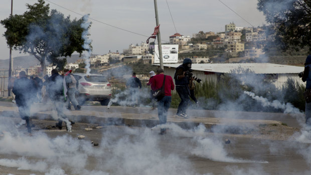 Palestinian demonstrators run from tear gas fired by Israeli troops during clashes after a demonstration  at Hawara checkpoint near the West Bank city of Nablus, on Sunday.