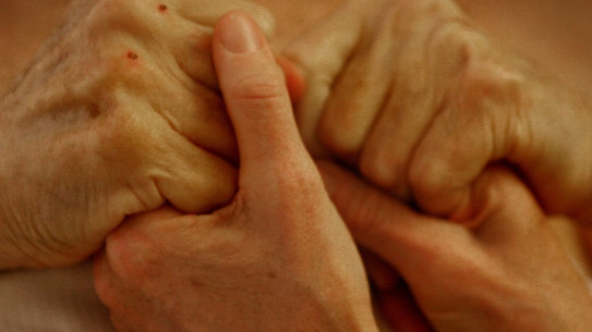 Sydney couple, Anjelika Elliott holds her husband Dr John Elliott’s hands as he attempts to rise from his hotel room bed in Zurich 26 hours before going to the Dignitas clinic where he ended his life in 2007.