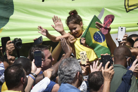 Brazil's President Jair Bolsonaro, left of girl, greets supporters outside the presidential palace in Brasilia, during a daily "door stop".