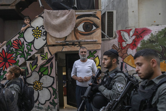 Israeli police officers walk past Nasser Rajabi as he stands outside the house that he shares with Jewish settlers in East Jerusalem.