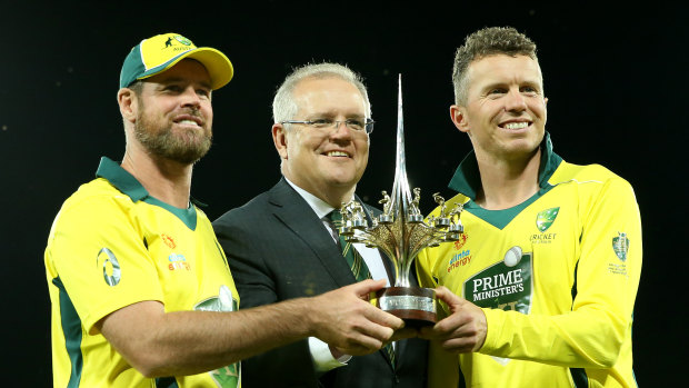 Prime Minister Scott Morrison holds a trophy with PM XI’s co-captains Dan Christian and Peter Siddle in 2019.