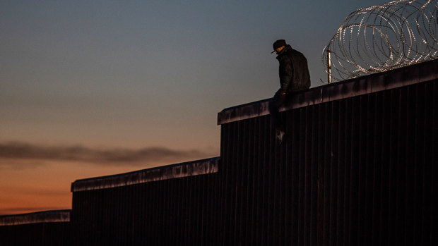 A man sits on top of an existing section of a US-Mexico border wall at dusk in Tijuana, Mexico.