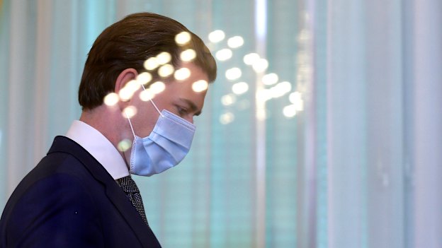 Austrian Chancellor Sebastian Kurz walks with a protective mask behind a reflective shield at the federal chancellery in Vienna.
