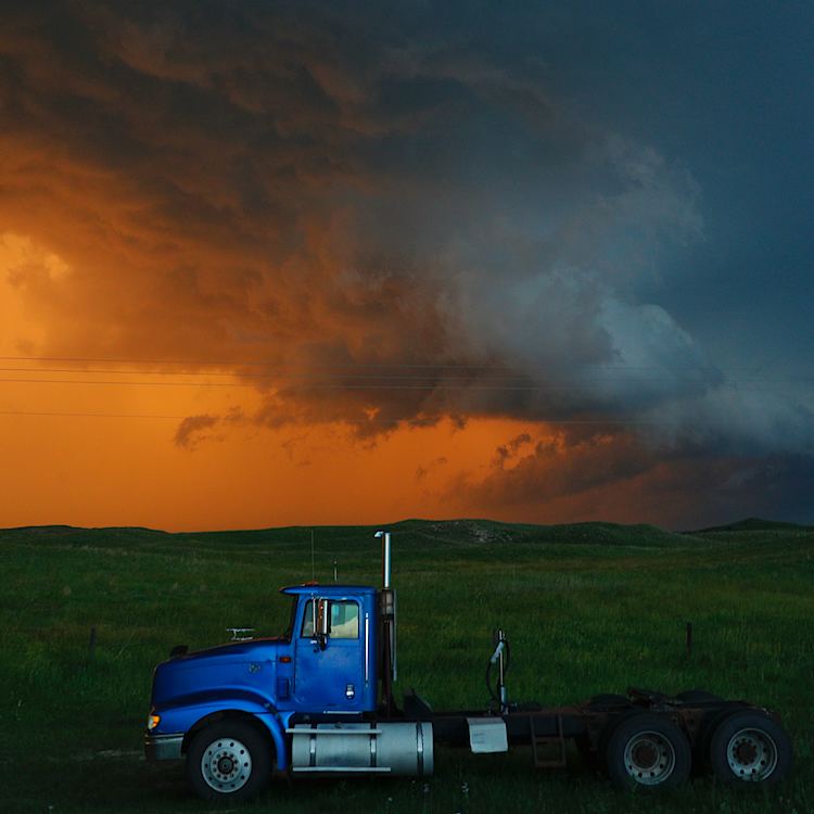 A truck travels on as storms colour the background.