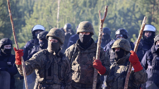 Polish police and border guards stand near barbed wire to stop migrants from the Middle East and elsewhere gathering at the Belarus-Poland border.