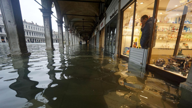 A shopkeeper looks out of his shop at a flooded St Mark's Square from behind a flood-protection barrier.