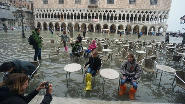 Tourists pose for photos in flooded St Mark's Square.