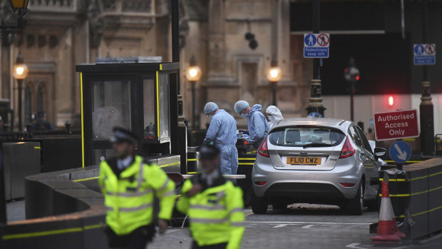 As darkness falls, forensic officers work by the car that crashed into security barriers outside the Houses of Parliament.