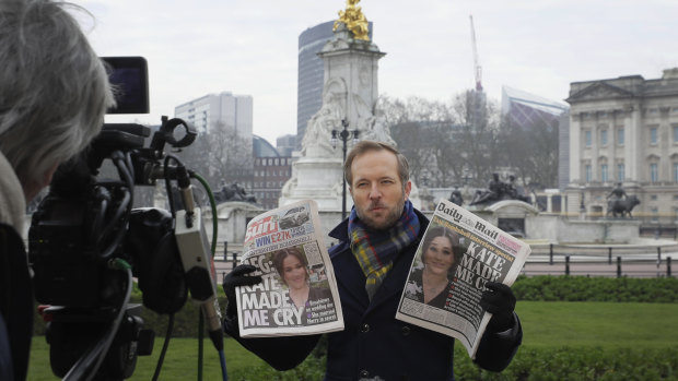 A television journalist holds up two British newspapers as he speaks to camera outside Buckingham Palace.