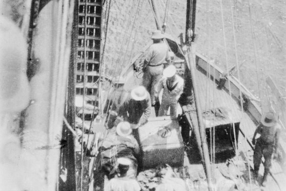 A wounded Brian Pockley, his face shielded by a pith helmet, being brought aboard the  Australian force’s ship.