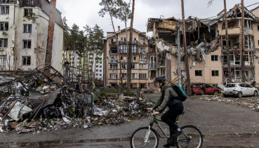 Un bărbat se plimbă cu bicicleta lângă clădirile distruse din Irbin, Ucraina. 
