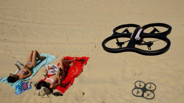 A remote controlled drone helicopter above sun bathers.