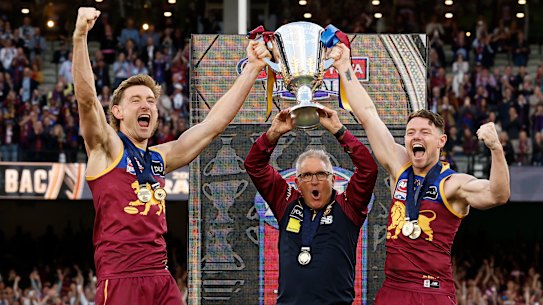 Co-captains Harris Andrews (left) and Lachie Neale (right) lift the premiership cup with Brisbane Lions coach Chris Fagan.