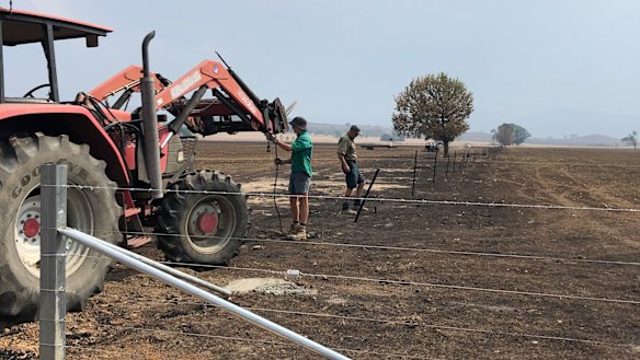 Tom Sheather (foreground) helps his uncle repair fences on his family’s burnt farm.