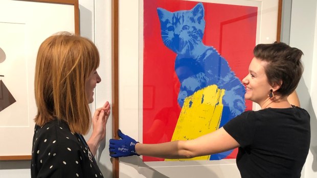 Rebecca Richards, left, and Emilie Patteson,  from the Australian Parliament House art collections team check Meow, a work by Maria Kozic, on display in the Imprint exhibition. 