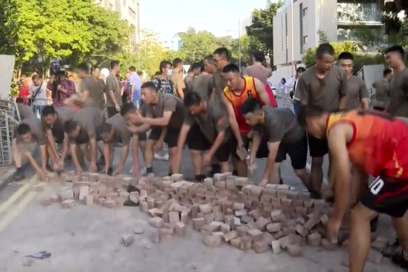 In this image made from video, People’s Liberation Army soldiers dressed in shorts and T-shirts pick up bricks scattered by protesters at Hong Kong Baptist University in Hong Kong, on Saturday. 