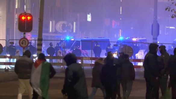 A group of pro-Palestinian protesters walk toward police line, with police vans driving in the background, near the soccer stadium in Amsterdam, Netherlands.