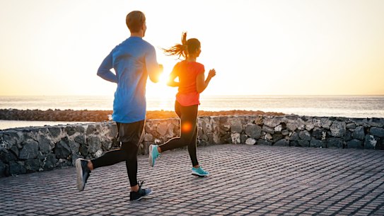 Health young couple jogging together next the ocean during a magnificent sunset - People work out on the beach.