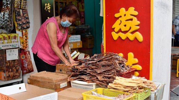 A vendor wearing a face mask prepares to display traditional Chinese medicinal products.
