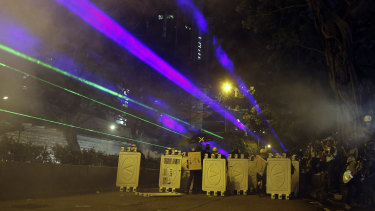 Protesters huddle behind barriers and use laser beams to shine at riot police during confrontations in Tsim Sha Tsui in Hong Kong