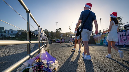 Beachgoers pass by flowers and candles left in memory of those who died in the Bondi massacre.