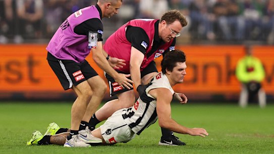Lachie Schultz of the Magpies collapses in the hands of medical staff.