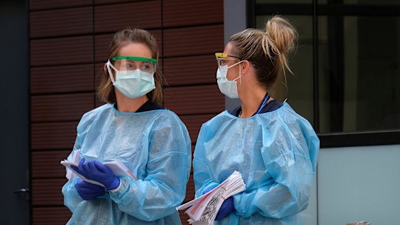 Hospital staff assist people waiting in line to be screened for COVID-19 outside the Royal Melbourne Hospital.