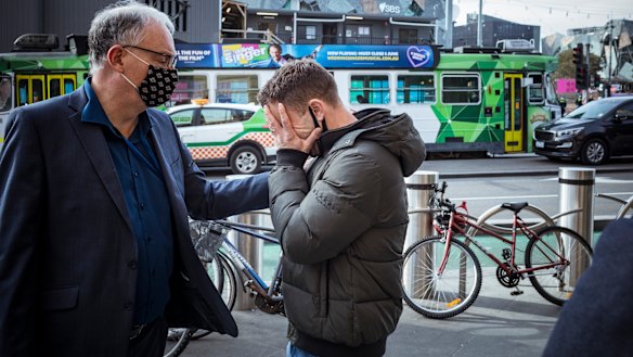 Small business owner Bill Panayotou is comforted after he got emotional talking about his business woes during lockdown outside Flinders Street Station.