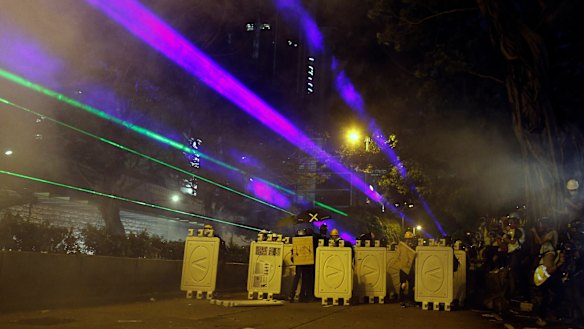 Protesters huddle behind barriers and use laser beams to shine at riot police during confrontations in Tsim Sha Tsui in Hong Kong