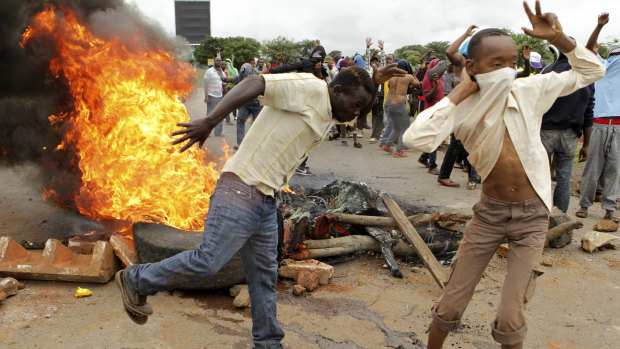 Protesters gather near a burning tire during a demonstration over the hike in fuel prices last week. The President has returned to Zimbabwe, seeking to restore "calm".