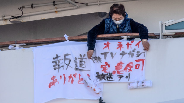 A Diamond Princess passenger hangs a banner reading "please broadcast this on TV" next to one (left) reading "thank you for reporting this".